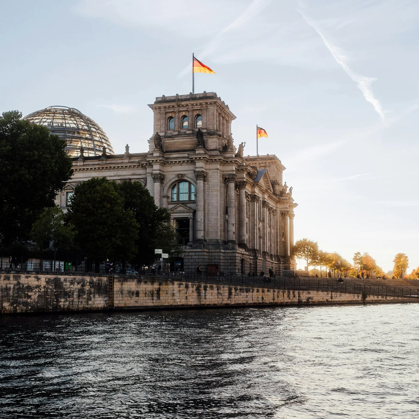 Berliner Sehenswürdigkeiten Reichstagsgebäude mit deutschen Flaggen und Fluss im Vordergrund bei Sonnenuntergang