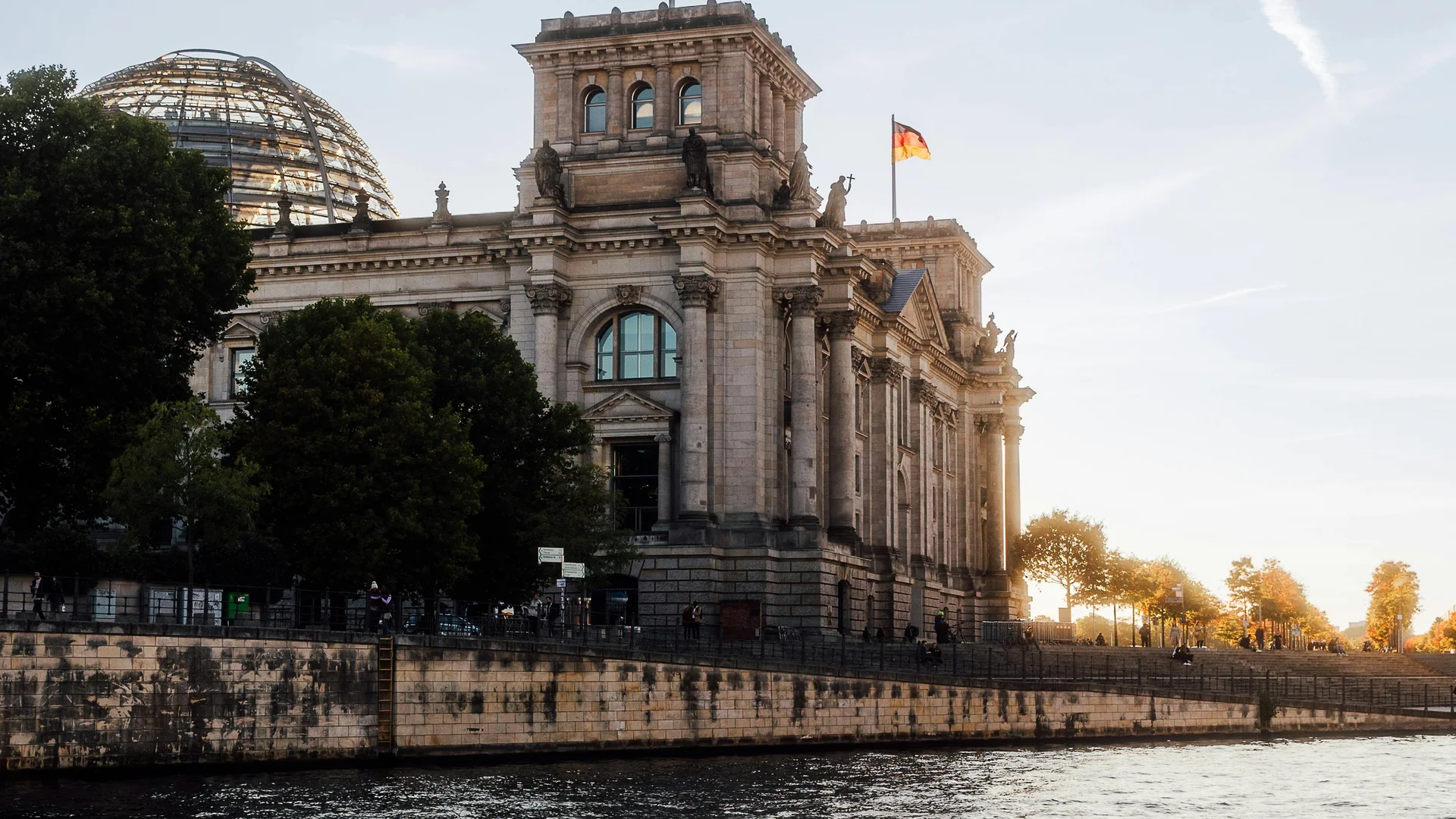 Bilder aus dem DASEYN Reichstagsgebäude mit deutschen Flaggen und Fluss im Vordergrund bei Sonnenuntergang