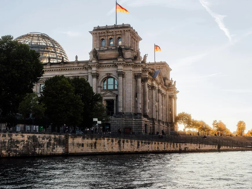Berliner Sehenswürdigkeiten Reichstagsgebäude mit deutschen Flaggen und Fluss im Vordergrund bei Sonnenuntergang