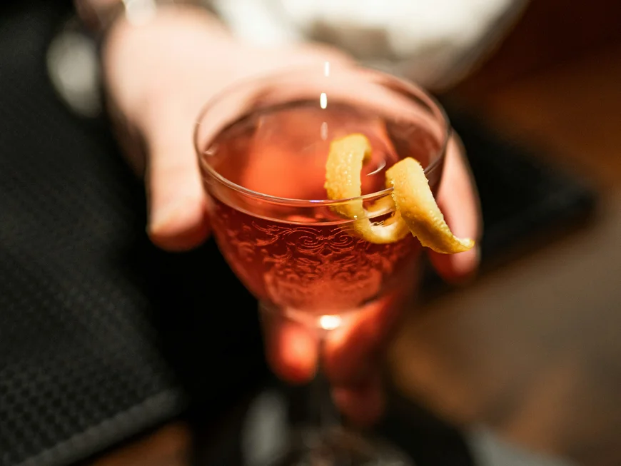 Workation in Berlin im DASEYN Hand hält ein Glas mit rotem Cocktail und Zitronenschale