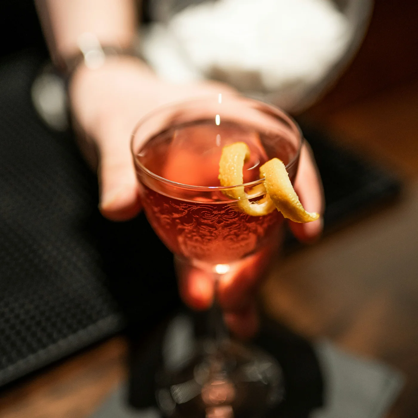 Workation in Berlin im DASEYN Hand hält ein Glas mit rotem Cocktail und Zitronenschale