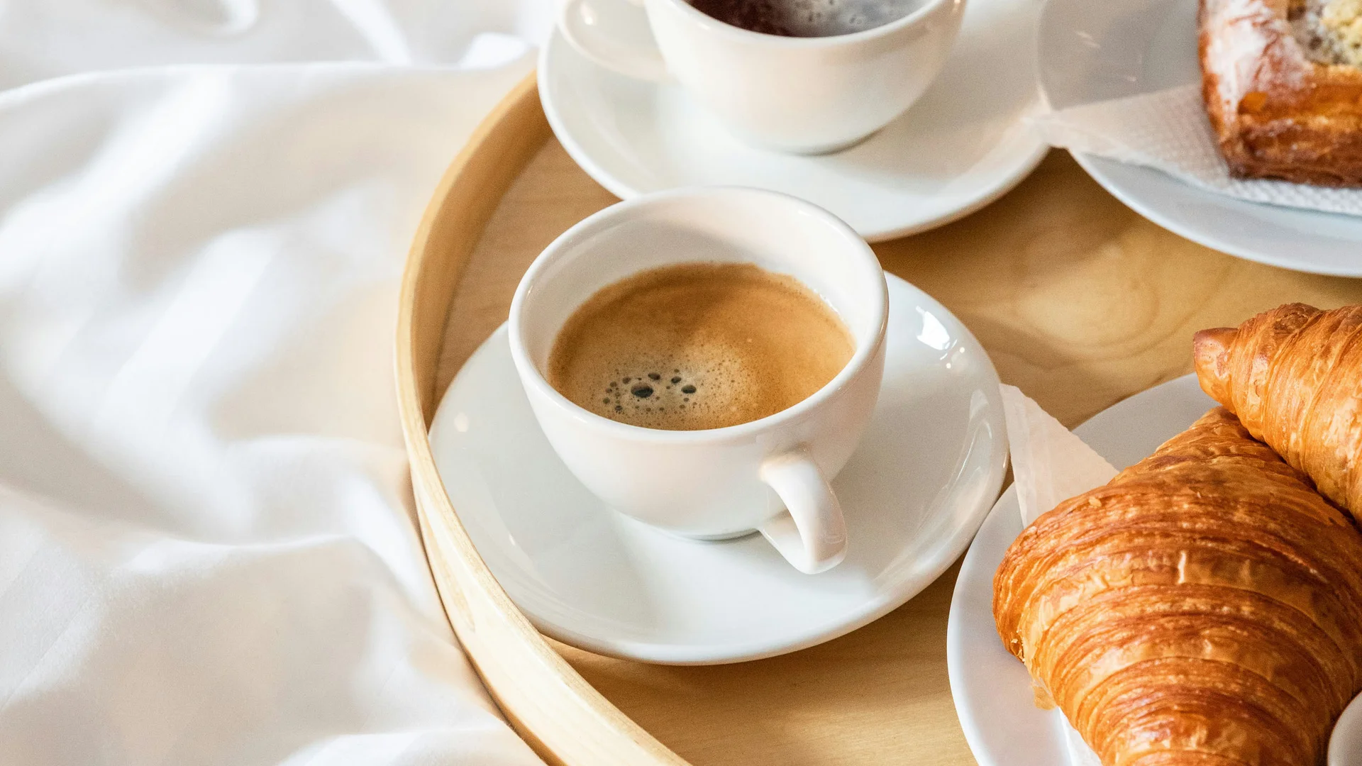 Bilder aus dem DASEYN Frühstückstablett mit Kaffee und Gebäck auf weißer Bettdecke