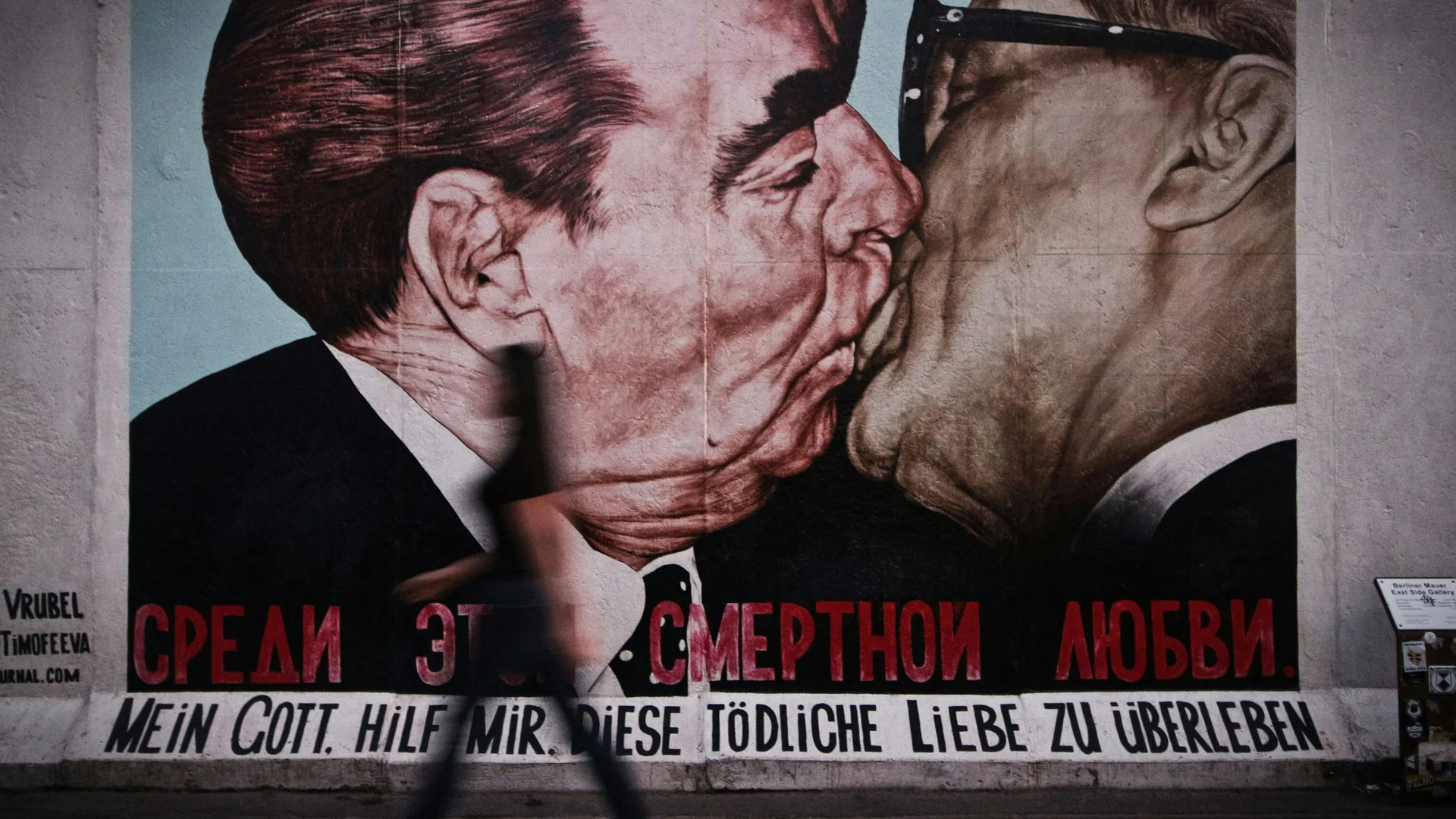 Bilder aus dem DASEYN Wandgemälde zeigt zwei Männer, die sich küssen, mit Person im Vordergrund