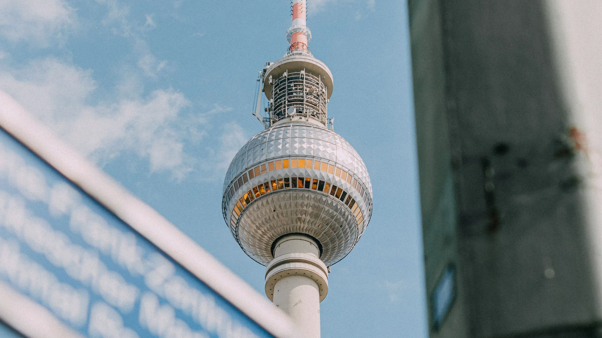 Bilder aus dem DASEYN Berliner Fernsehturm mit blauem Straßenschild im Vordergrund bei klarem Himmel