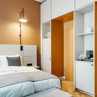 Ihr Stadthotel in Berlin: DASEYN | Fischerinsel Modernes Schlafzimmer mit weißen Möbeln und orangefarbenen Wänden