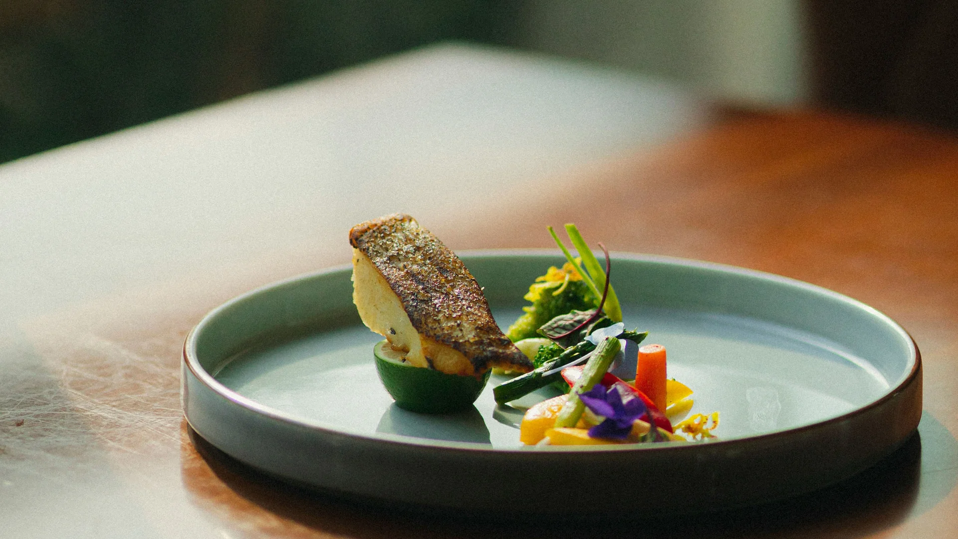 Bilder aus dem DASEYN Kunstvoll angerichteter Fisch mit Gemüse und essbaren Blüten auf grünem Teller