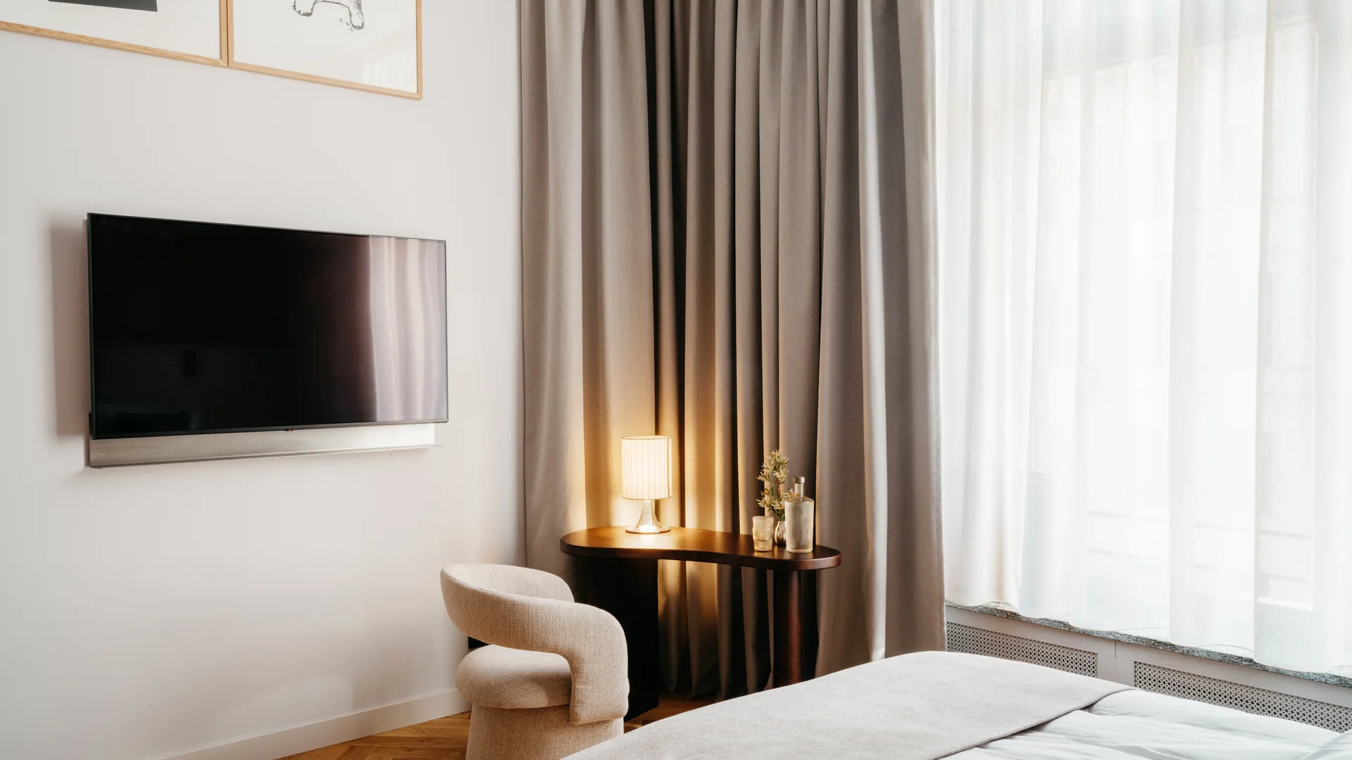 Bilder aus dem DASEYN Modernes Hotelzimmer mit Fernseher, gemütlichem Stuhl und Vorhängen