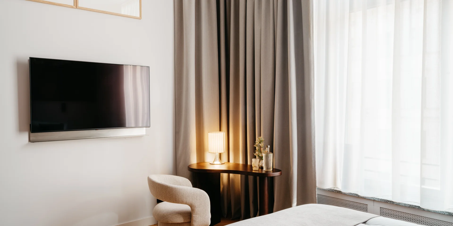 Modernes Hotelzimmer mit Fernseher, gemütlichem Stuhl und Vorhängen