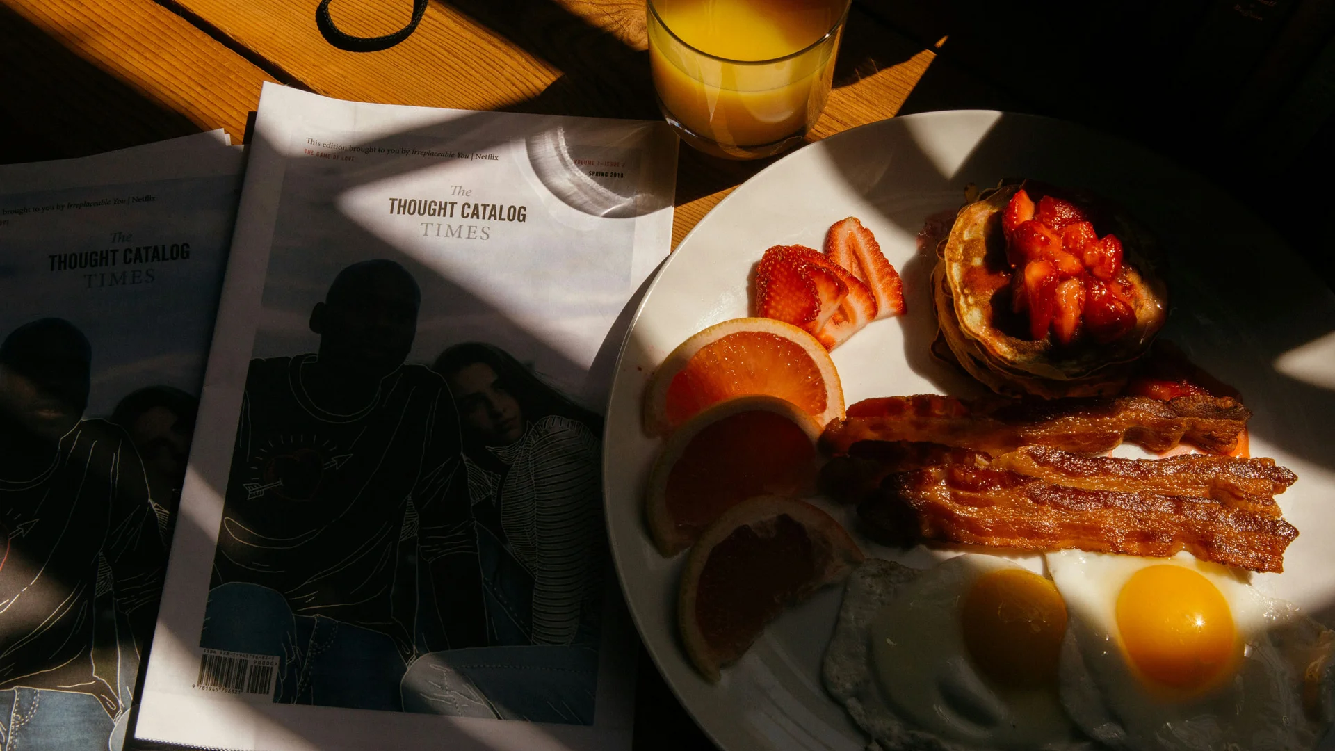 Bilder aus dem DASEYN Frühstücksteller mit Speck, Spiegeleiern, Obst und Orangensaft auf Holztisch