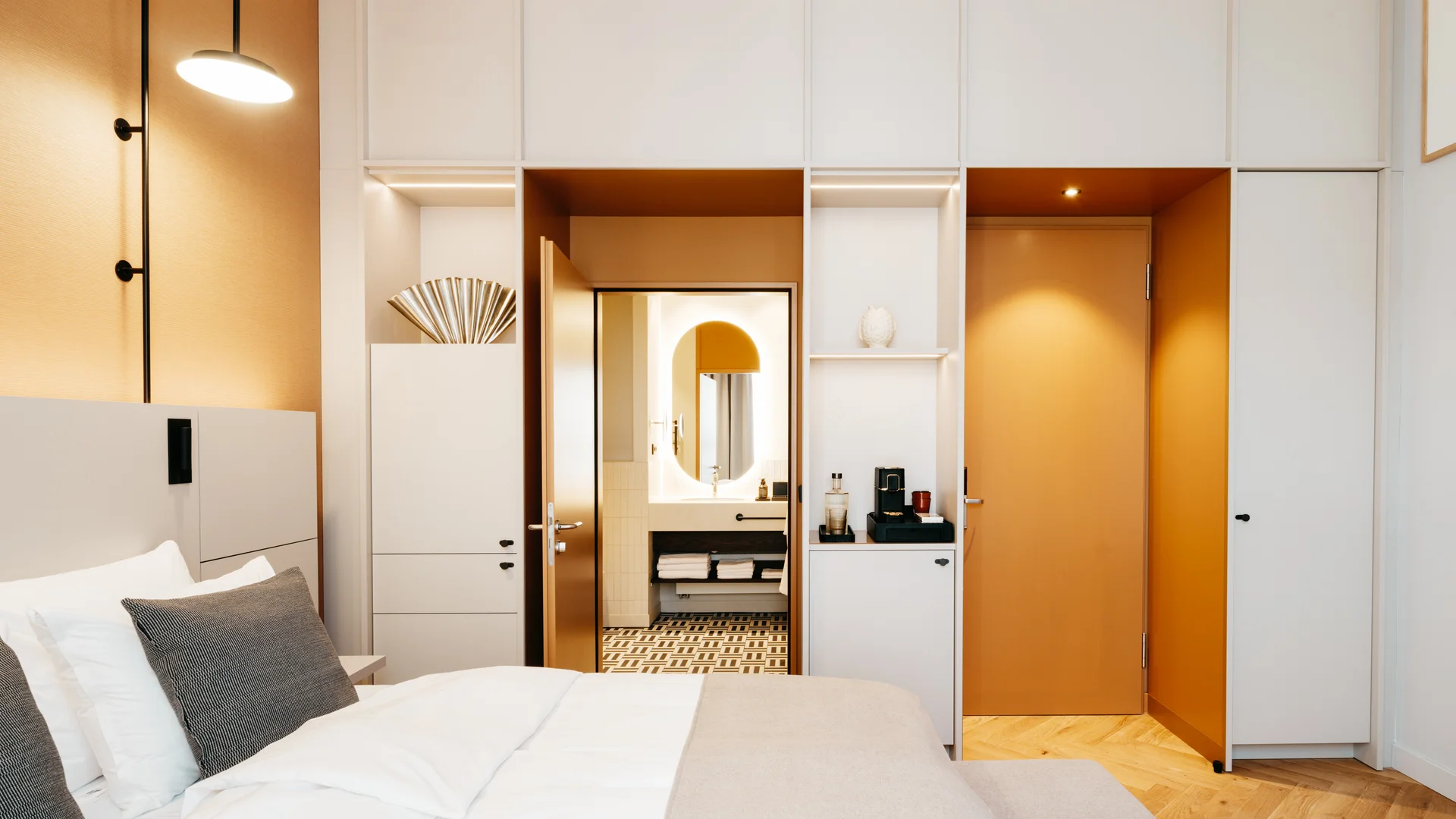 Bilder aus dem DASEYN Modernes Hotelzimmer mit weißem Bett, grauen Kissen und offenem Bad