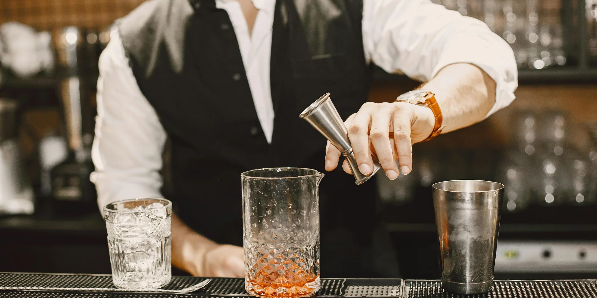Jobs im Hotel in Berlin: Arbeiten im DASEYN Barkeeper gießt Flüssigkeit mit Messbecher in Cocktailglas an der Bar