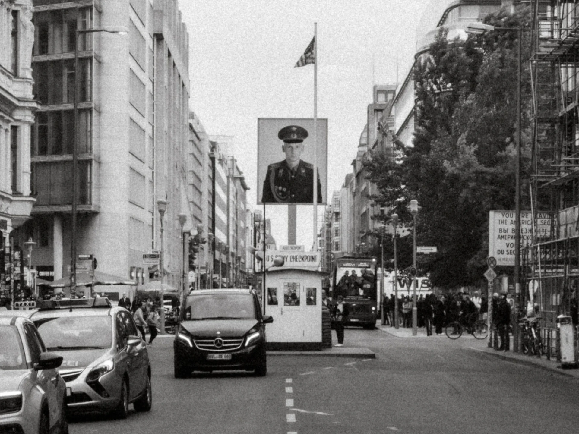 Historische Stadtstraße mit Kontrollhäuschen, Autos und großem Porträt an einer Fahnenstange